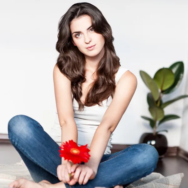 Thoughtful young woman sitting with red flower — Stock Photo, Image