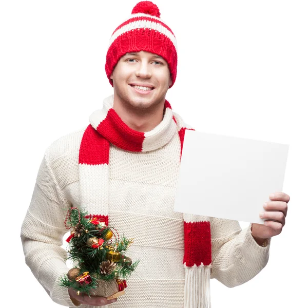 Young casual man in winter hat hoding christmas tree and sign — Stock Photo, Image