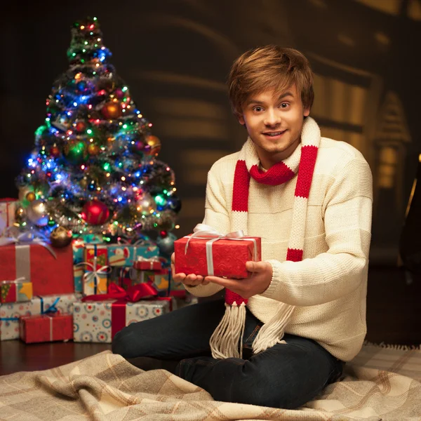 Joven hombre sonriente sosteniendo regalo de Navidad rojo —  Fotos de Stock