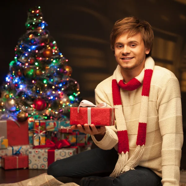 Young smiling man holding red christmas gift — Stock Photo, Image