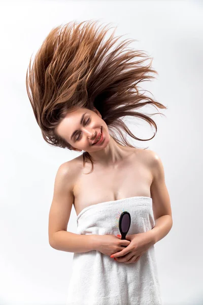 Όμορφη γυναίκα με χαμόγελο κρατά μια βούρτσα μαλλιών σε λευκό φόντο. τρίχωμα που πετάει — Φωτογραφία Αρχείου