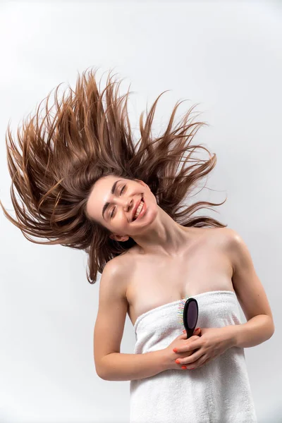 Schöne Frau mit einem Lächeln hält eine Haarbürste auf weißem Hintergrund. Haarfliegen — Stockfoto