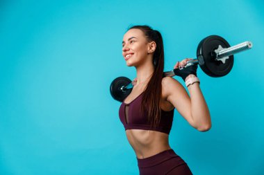 Güzel, sportif esmer kadın mavi arka planda halterini omuzlarında tutuyor. izole