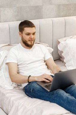 Evdeki kanepede dizüstü bilgisayarı olan genç adam.