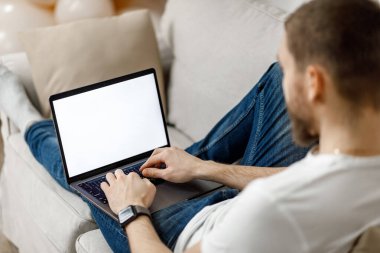 Evdeki kanepede dizüstü bilgisayarla çalışan bir adamın yakın çekimi. Yüzü yok.