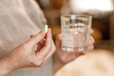 Bir hap ve bir bardak su tutan son sınıf bayan elleri..