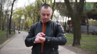 Şehir parkında akıllı saati olan yakışıklı bir genç. Bahar.