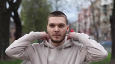 Genç adam bej kapüşonlu bir kapüşon giyer ve ellerini ovuşturur.