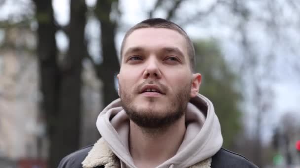 Молодий чоловік одягає навушники під час ходьби в міському парку. туристичний — стокове відео