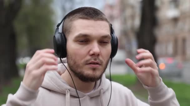 Молодий чоловік знімає навушники під час прогулянки в міському парку. туристичний — стокове відео