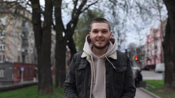 Jeune homme met des écouteurs tout en marchant dans le parc de la ville. touriste — Video