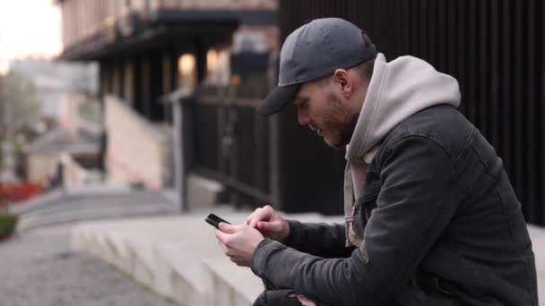 Випадковий чоловік використовує смартфон, сидячи в місті — стокове відео