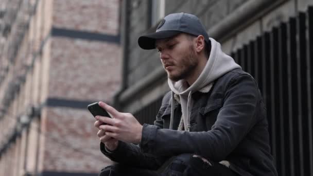 Casual man using smartphone while sitting in the city — Vídeo de stock