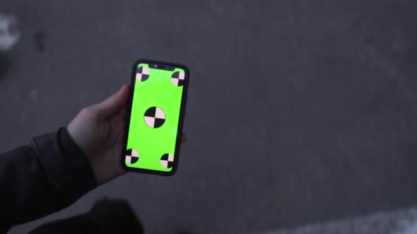 POV, male hand holding smartphone with blank green screen chromakey walking in car parking — Stockvideo