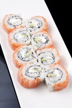 siyah arka plan üzerinde beyaz bir tabağa Japon suşi rulo
