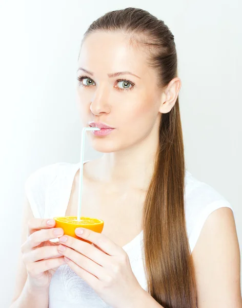 Attractive smiling young woman drinking orange juice straight from fruit — Stock Photo, Image