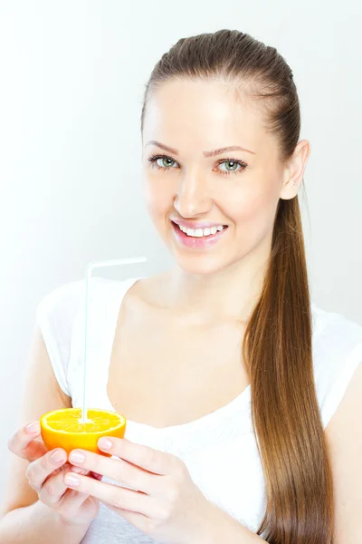 Attrayant sourire jeune femme qui boit du jus d'orange directement à partir de fruits — Photo