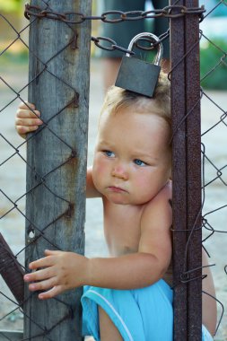 Locked baby boy trying to escape through wire fencing with padlo clipart