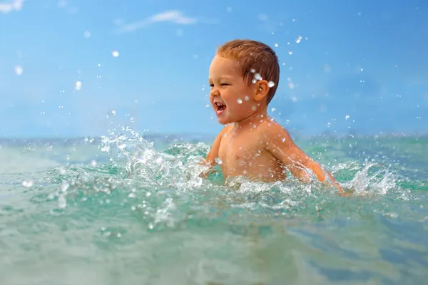 Gelukkig babyjongen maken water spatten in de zee — Stockfoto