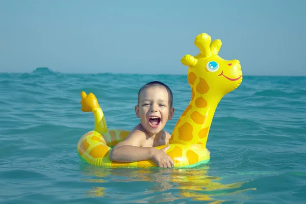 Feliz niño riendo disfrutando de nadar en el mar con jirafa anillo de goma —  Fotos de Stock