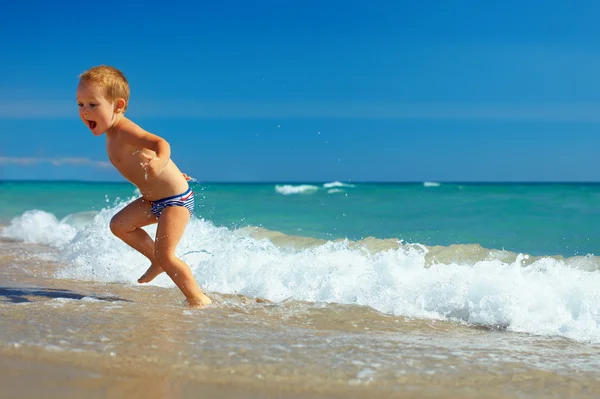 Χαριτωμένο παιδί που τρέχει από τα κύματα της θάλασσας στην παραλία — Φωτογραφία Αρχείου