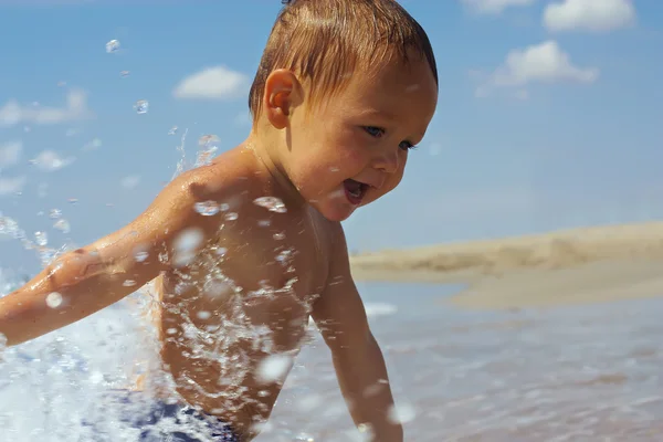 Mooie actieve baby spelen met zeewater op het strand — Stockfoto