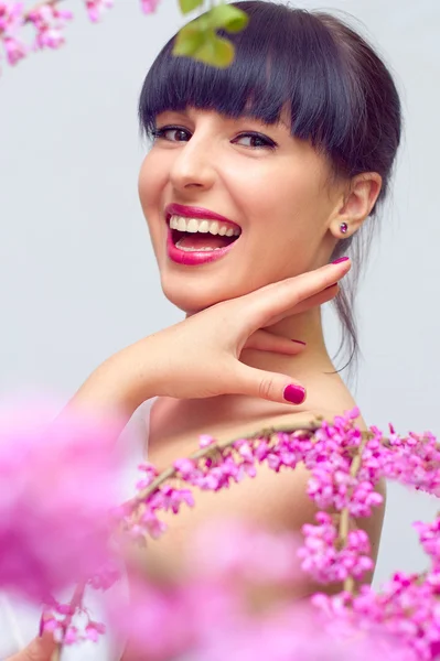 Bela mulher sorridente entre flores cor de rosa — Fotografia de Stock