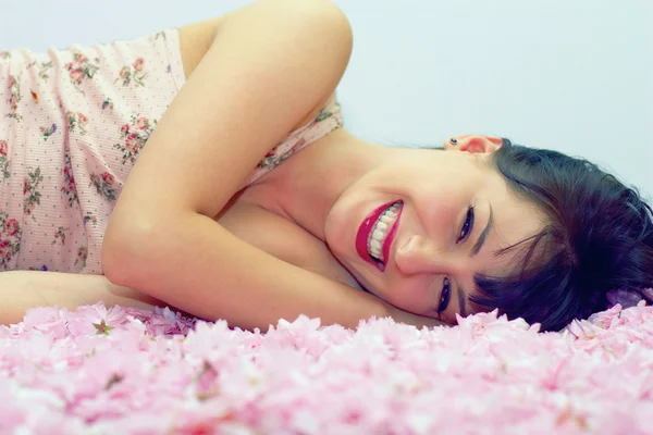 Mooie lachende vrouw liggen in bloemblaadjes — Stockfoto