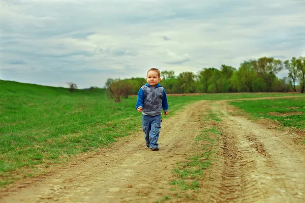 Kleine babyjongen lopen landweg op bewolkte hemelachtergrond — Stockfoto