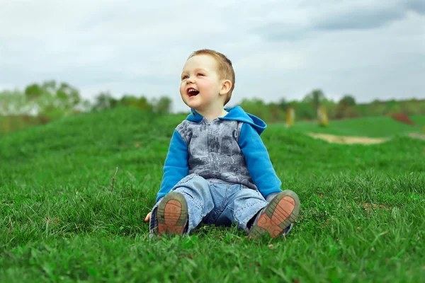 Feliz rindo menino sentado no campo verde — Fotografia de Stock