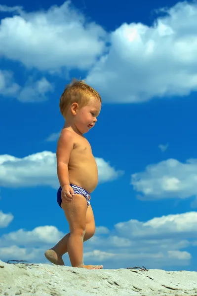 Bayi laki-laki lucu berjalan di pantai di langit berawan latar belakang. tampilan bawah — Stok Foto