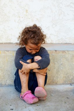 Beton duvara oturan fakir, üzgün küçük kız çocuk