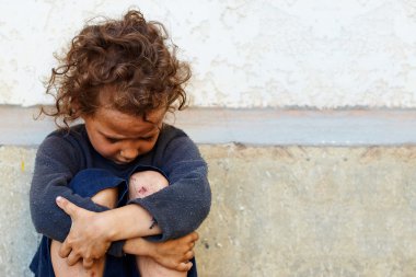 Beton duvara oturan fakir, üzgün küçük kız çocuk