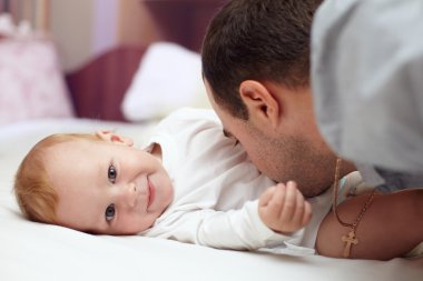 bebekle oynayan genç mutlu baba. adam ve bebek yatakta yatarken. Bebek