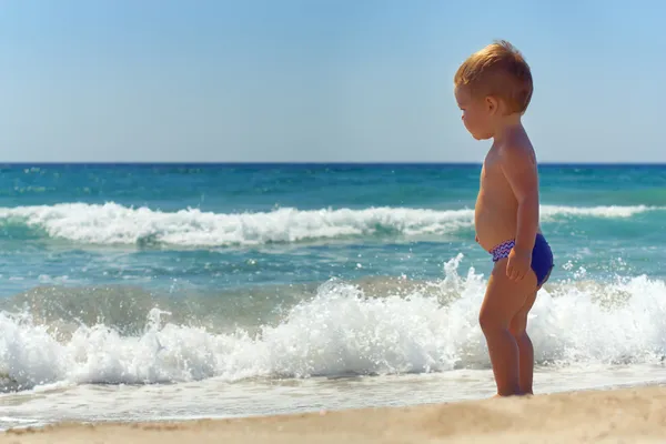 Lindo bebé niño de pie en olas en la playa — Foto de Stock