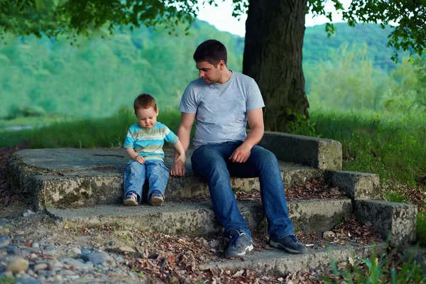 Padre e hijo sentado en las escaleras debajo de un árbol viejo. lazos familiares —  Fotos de Stock