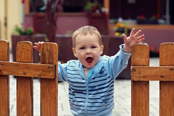 Söt pojke står i en öppen trästaket med en Välkommen expressio — Stockfoto