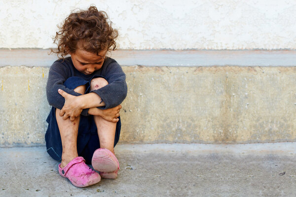 Бедная, грустная маленькая девочка сидит у бетонной стены
