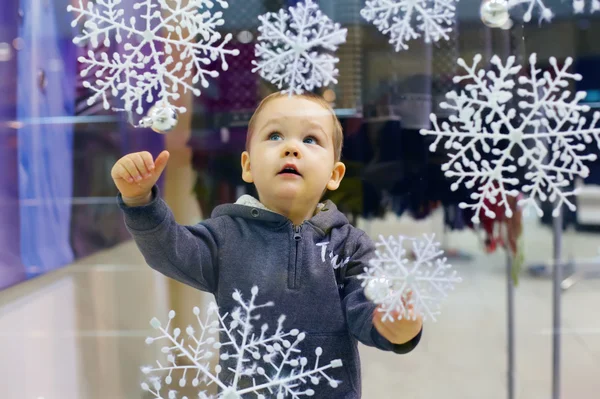 Curious little baby boy looking at snowflakes on shop window in city mall — Stock Photo, Image