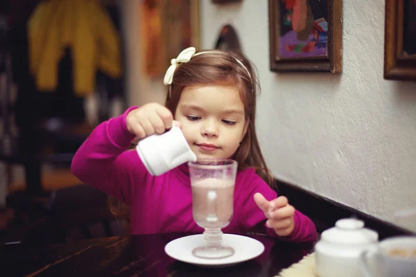 Adorabile bambina che versa la panna nel cappuccino. caffè al coperto — Foto Stock