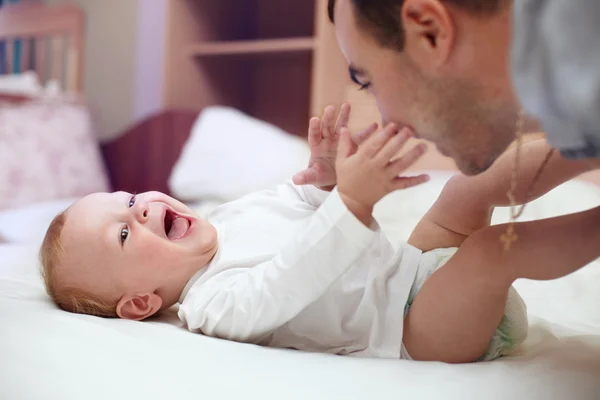 Ung glad pappa leker med barnet. mannen och barnet ligger i sängen. Baby — Stockfoto