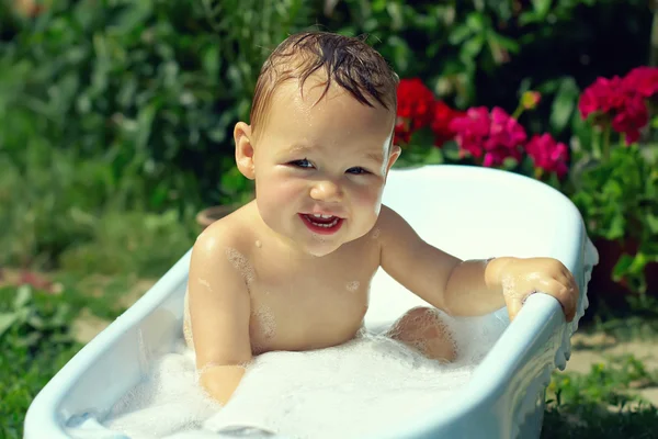 Cute funny small baby boy bathing outdoor on green lawn among flowers — Stock Photo, Image