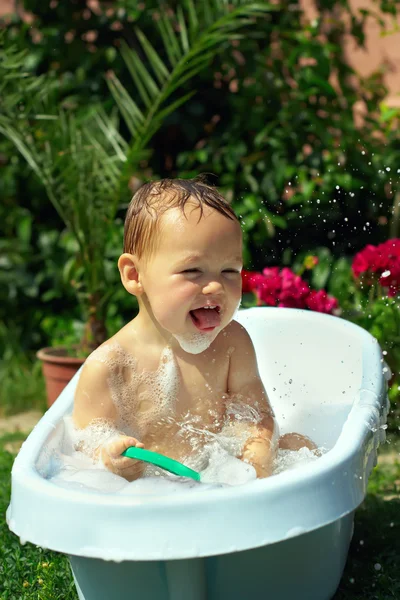 Lindo niño divertido bañarse al aire libre en césped verde entre las flores —  Fotos de Stock