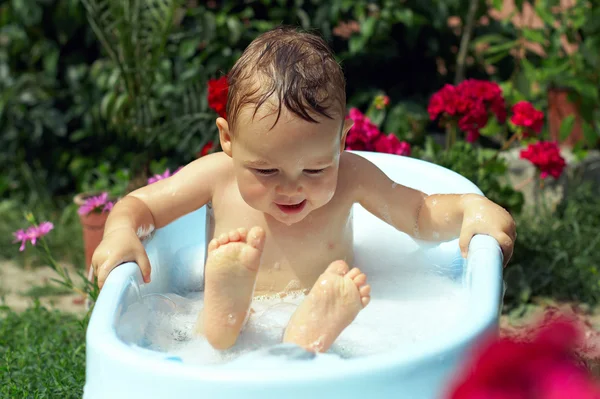 Милый забавный маленький мальчик купается на открытом воздухе в зеленом саду — стоковое фото