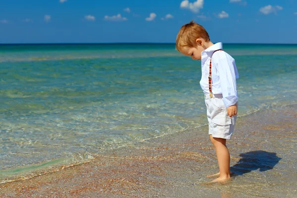 Dreamy baby boy stands in surf on sea beach — Stock Photo, Image