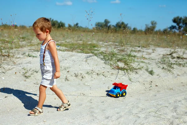 Cute baby boy dragging toy car walking at the field — Stock Photo, Image