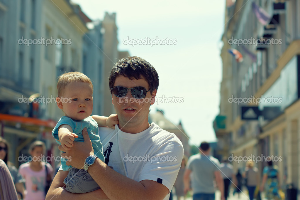 Father with child on hands walking through crowd outdoor in the city