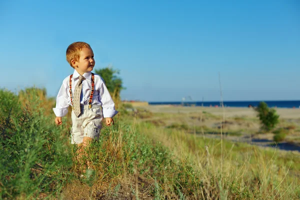 Business-Stil Baby Junge zu Fuß durch das Feld in der Nähe des Meeres — Stockfoto