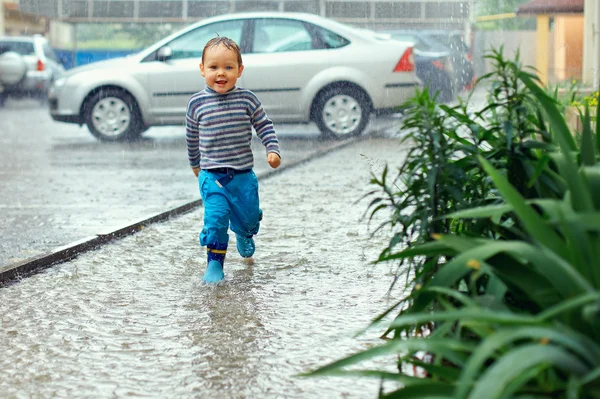 Милий хлопчик біжить під водійським дощем — стокове фото