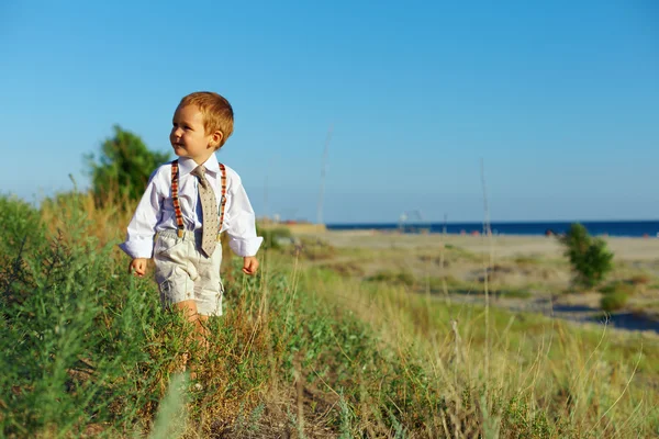 Bambino in stile business che cammina attraverso il campo vicino al mare — Foto Stock